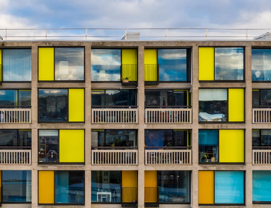 A restored building, with brightly coloured panels of yellow and orange, large glass windows and a restored concrete frame